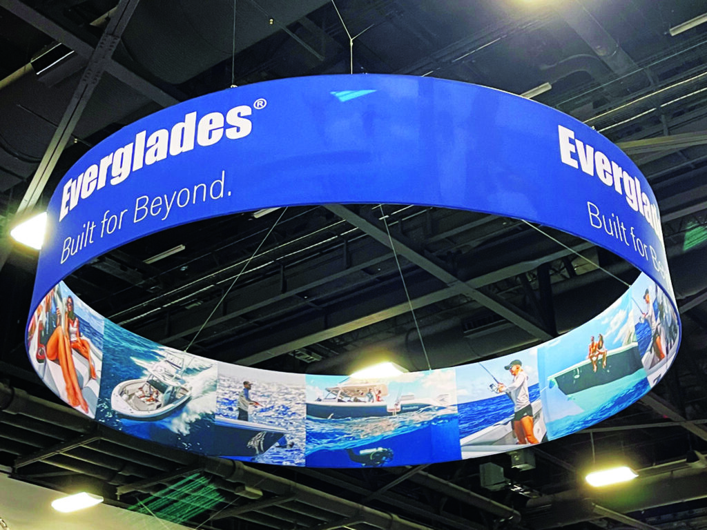 Large overhead trade show sign suspended above a branded exhibit area